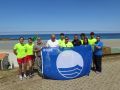 Socorristas y representantes del gobierno local posando con la bandera azul antes de izarla en la playa de Caión