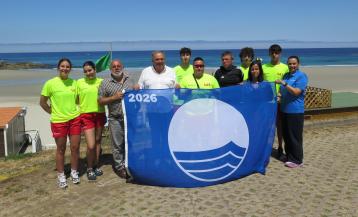 Socorristas y representantes del gobierno local posando con la bandera azul antes de izarla en la playa de Caión