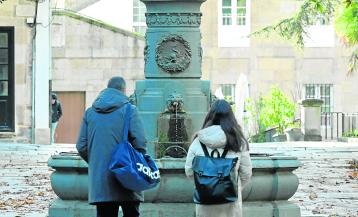 Dos transeúntes observan la fuente sin la estatua, ayer