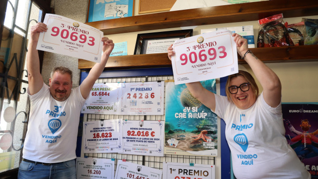 Fernando Montero Valiña y su hermana Sara posando con la tradicional camiseta y el cartel con el número del que vendieron tres décimos en su establecimiento de Baio
