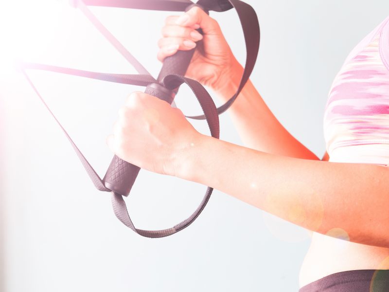 Fitness femenina en sujetador de deporte rosa con las manos en trx copiar el espacio