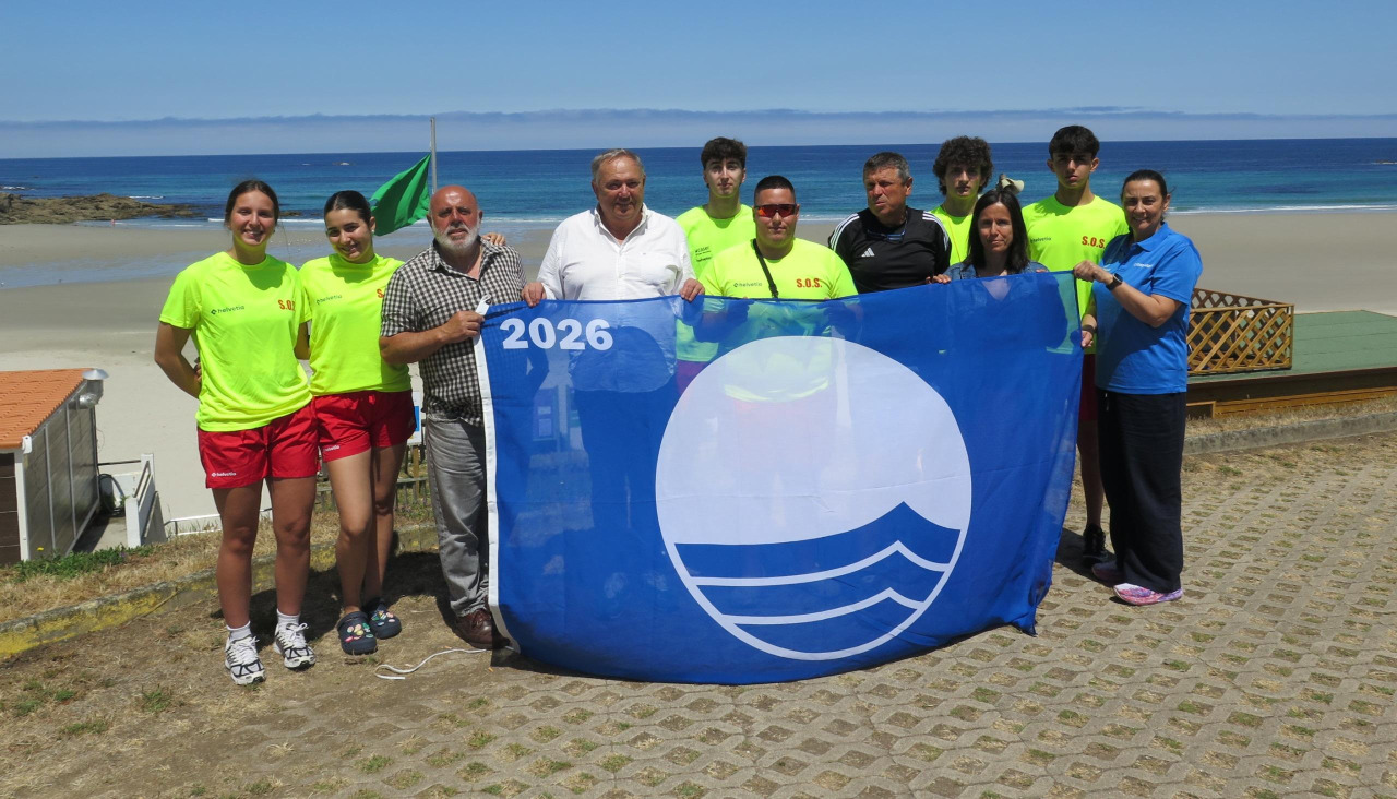Socorristas y representantes del gobierno local posando con la bandera azul antes de izarla en la playa de Caión