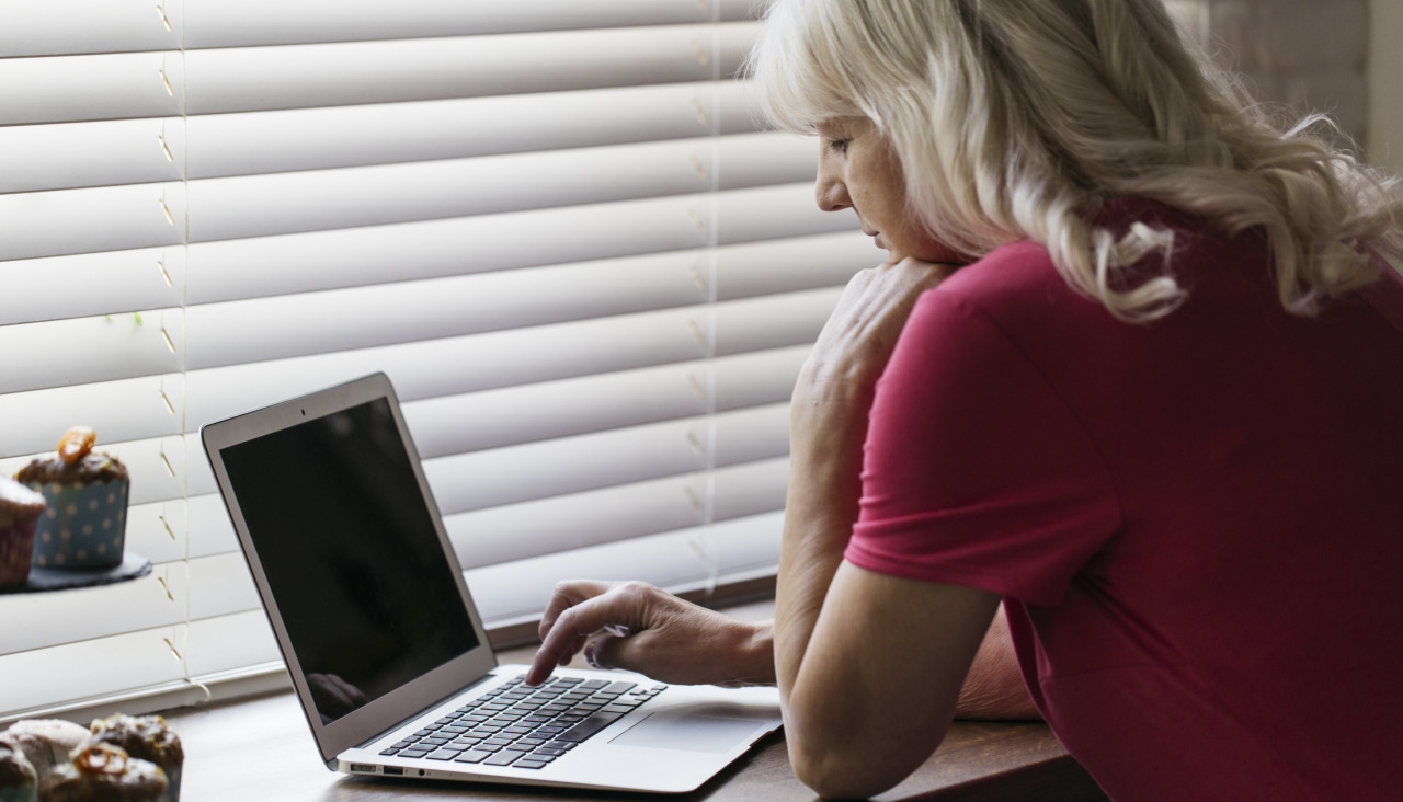 Mujer madura que usa la computadora portatil cerca de la ventana
